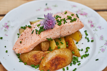 Close up picture on poached salmon with baked new not peeled potatoes and chopped chives served on rustic porcelain plate. Tasty healthy dish, full of nutritions and protein ideal for balanced diet.
