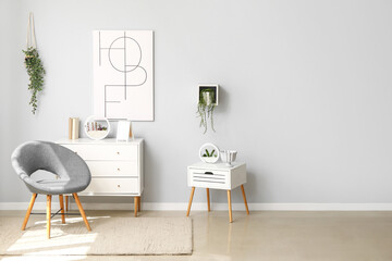 Interior of light living room with cozy grey armchair, chest of drawers and table