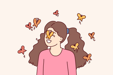 Little girl among butterflies flying and landing on face for spring mood concept. Happy childhood of preteen girl loving animals and laughing at sight of butterflies in summer park