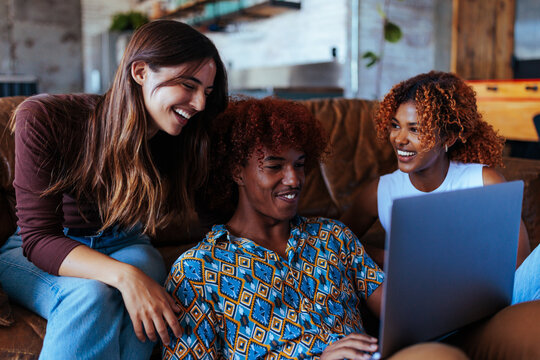 Three young people using laptop together in living room