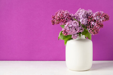 Vase with beautiful lilac flowers on light table against color background
