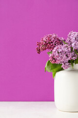 Vase with beautiful lilac flowers on light table against color background