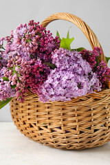 Fototapeta na wymiar Wicker basket with aromatic lilac flowers on light table, closeup
