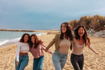 Multiracial group of four young women running on beach during rainy day