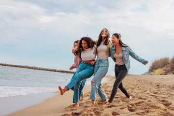 Four young women jumping together on beach - 607510845