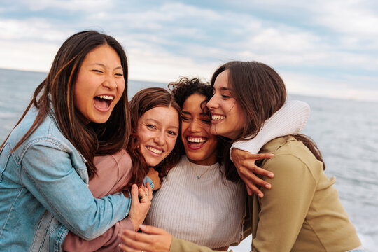 Portrait of four young women laughing and hugging on beach