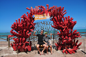 turistas pai e filho  na decoração de corais Maceió é massa  - obrazy, fototapety, plakaty