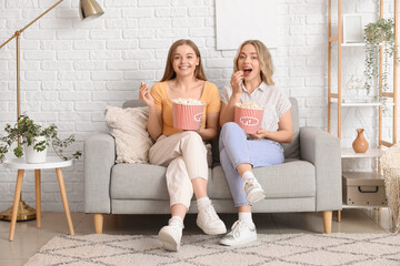 Young sisters eating popcorn on sofa at home
