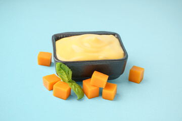 Bowl with tasty cheddar cheese sauce on blue background
