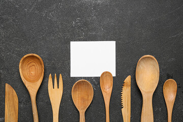 Composition with blank card and wooden cutlery on dark background