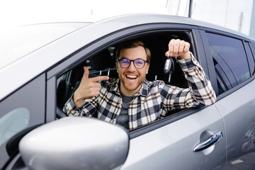 Excited young man showing a car key, sitting inside his new vehicle