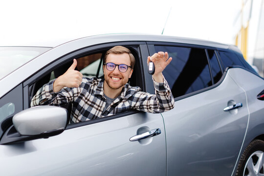 Excited young man showing a car key, sitting inside his new vehicle