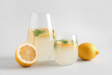 Glass and jug with fresh lemonade on grey background