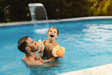 Playful father having fun with his little boy while being in swimming pool