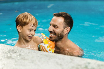 Playful father having fun with his little boy while being in swimming pool