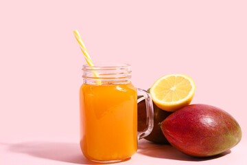 Mason jar of fresh mango smoothie and lemon on pink background