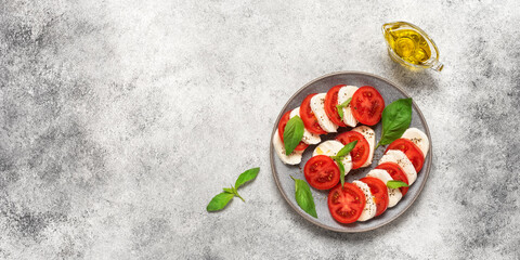 Italian Caprese salad with chopped tomatoes, mozzarella, basil, olive oil on a light stone background. Top view, flat lay. Banner