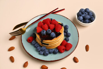 Plate with sweet pancakes, berries and nuts on beige background