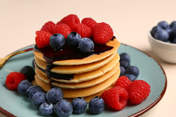 Plate with sweet pancakes and berries on beige background, closeup