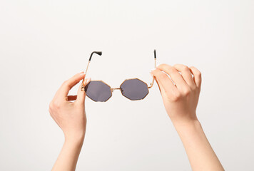 Female hands holding stylish sunglasses on white background