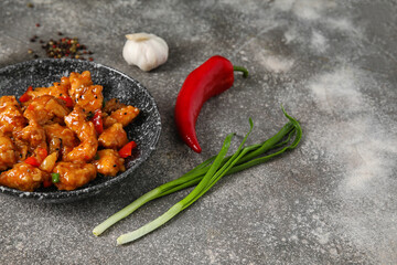 Tasty sweet and sour chicken in bowl with spices on grey background