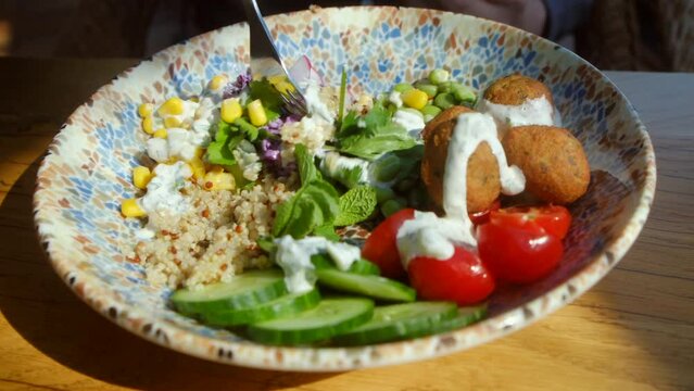 Close up mixing vegetable salad. Chickpea falafel salad with vegetables, quinoa and Edamame beans with Zaziki sauce on a wooden table. Vegetarian vegan food. High quality 4k footage. Bright, juicy
