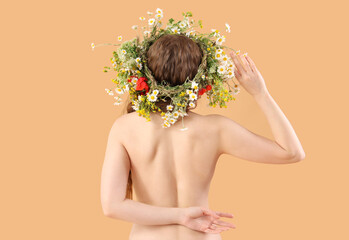 Beautiful naked young woman in flower wreath on beige background, back view. Summer solstice