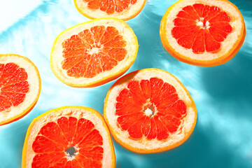 Slices of fresh grapefruit in water on blue background