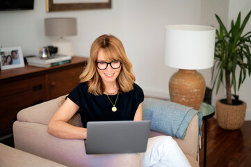 Attractive mid aged woman wearing casual clothes and using laptop at home
