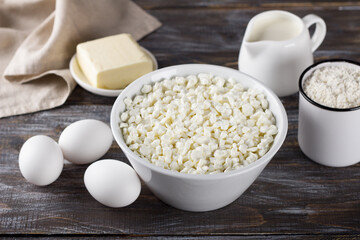 Bowl with cottage cheese, eggs, flour, butter, milk on a wooden background