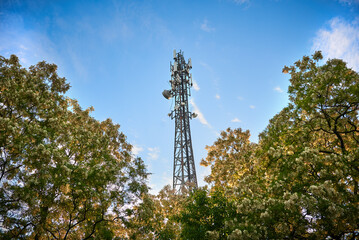 5G transmitter mast against the blue sky between the trees