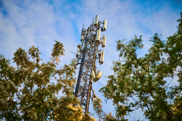 5G transmitter mast against the blue sky between the trees