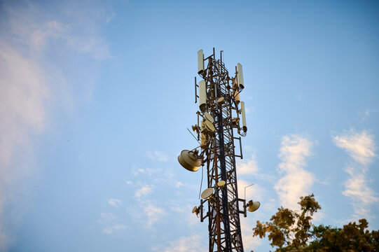 5G transmitter mast against the blue sky between the trees