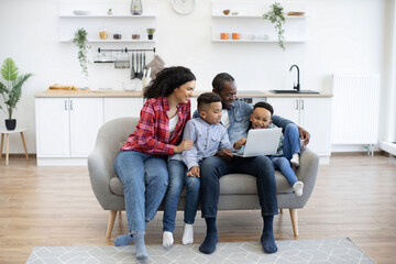 Full length view of multiethnic adults and boys looking at computer screen while sitting together...