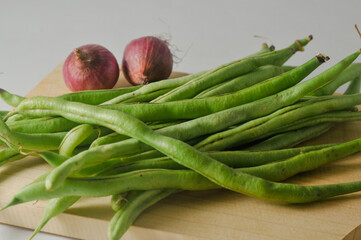 Some green beans and some red onions on a wooden cutting board isolated on a white background