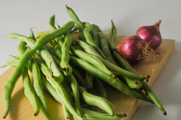 Some green beans and some red onions on a wooden cutting board isolated on a white background