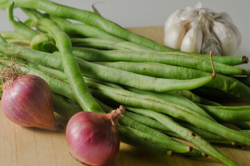Some green beans, some red onions and a garlic bulb on a wooden chopping board isolated on a white background