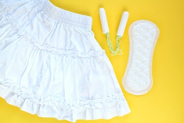 White skirt, woman sanitary pad and tampon swab on yellow background. Female menstruation cycle period. Hygiene concept. Linen and health protection idea. Copy space