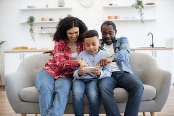 Inquisitive multiracial couple pointing fingers on phone screen held by calm little boy while...