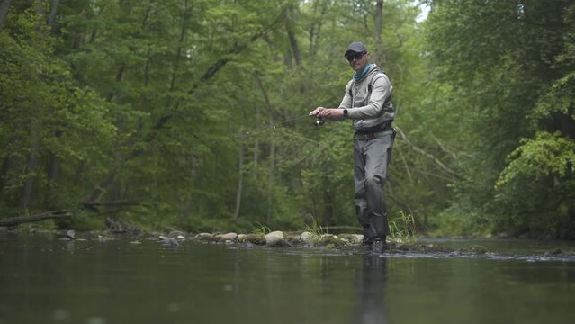 Fisherman catching brown trout on spinning tackle standing in river.