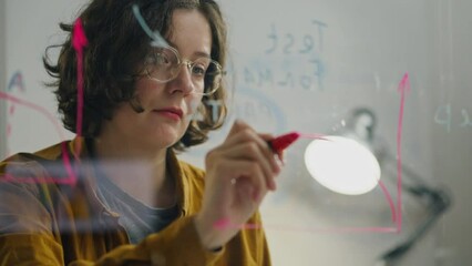 Notes, Medium business owner intently writes a note note using a glass wall in a corporate building. management consultant plans business strategy applying new methods of planning and organizing data