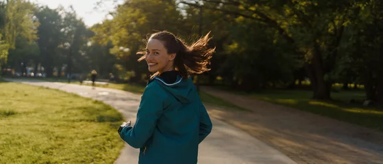  Portrait of smilling young woman running in the city park in the early morning. © Halfpoint