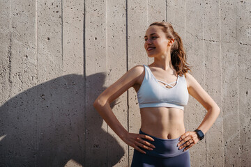Portrait of young sporty woman in sportswear excercising in front of concrete wall in the city. - obrazy, fototapety, plakaty