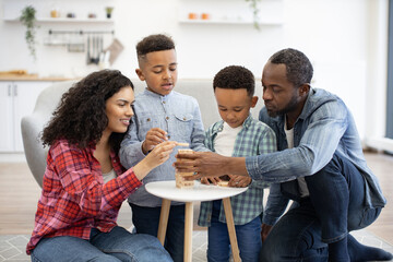 Naklejka premium Close up view of four-person family playing board game with wooden blocks on small table in living room. Happy people being engaged in enjoyable activity showing importance of love and care.