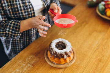 Happy redhead Woman making homemade cake with easy recipe, sprinkling powdered sugar on top. Icing sugar sprinkled with colander. Culinary, baking and cooking food concept