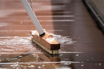 Detail of a scrubbing brush and sparkling water during spring cleaning of a wooden terrace floor.