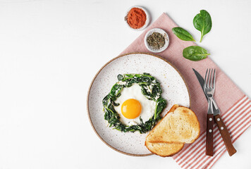 Fried eggs with fresh spinach and creamcheese on a plate on napkin on the white background, top view, copy space