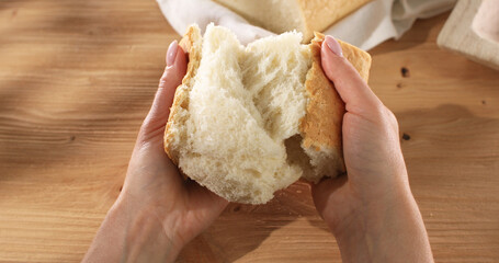 Female hands tear fresh bread. Texture of bread close up. Wooden background. Slow mation. Sunny day. First person view. 