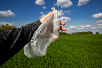 Plastic bag in hand on the background of a green field. Global problems with garbage. environmental pollution.