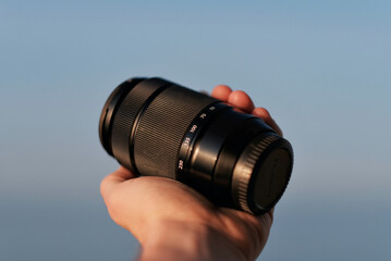 Zoom lens in the hands. 50mm-230mm. A palm holding a camera lens.